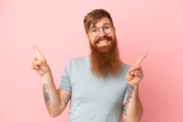 Young reddish caucasian man isolated on pink background pointing finger to the laterals and happy