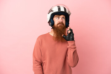Young reddish caucasian man with a motorcycle helmet isolated on pink background with fingers crossing and wishing the best