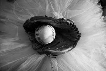 Baseball glove with softball in mid, sitting on top of a white ballet tutu.
