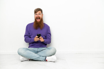 Fototapeta premium Young caucasian reddish man sitting on the floor isolated on white background surprised and sending a message