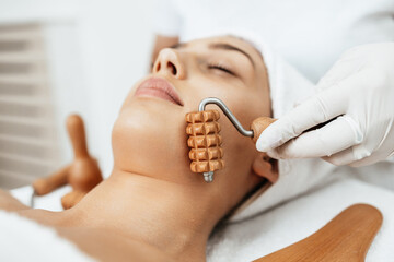 Beautiful brunette getting face maderotherapy in a beauty salon. Professional skin care treatment.