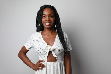 Smiling attractive young African woman with braids posing over white wall.