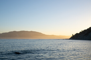 View across Tokomaru Bay in late afternoon as sun illuminates distant hills in golden glow