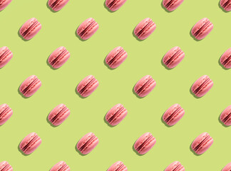 Pattern of pink macaron pastry french cookies on green background with hard light shadow.