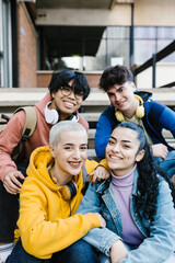 Vertical shot of multiracial young students sitting at school building entrance - Millennial people smiling at camera
