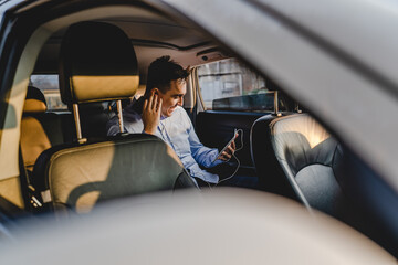 One man young adult caucasian manager or business director sitting on the back seat of the car while having online call conference using digital tablet to arrange business real people copy space