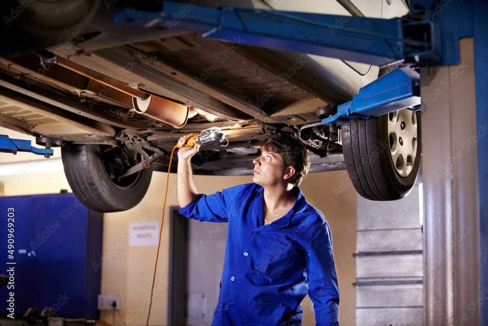 Wall mural getting some extra light. a young male mechanic using a light to look underneath a car.