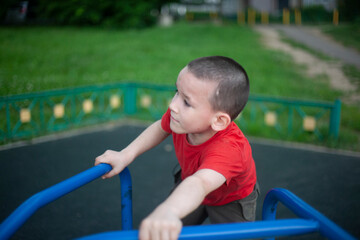 Fototapeta na wymiar Child on merry-go-round. Boy spins on carousel for children on playground. Junior schoolboy plays alone.