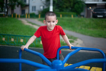 Child on merry-go-round. Boy spins on carousel for children on playground. Junior schoolboy plays...
