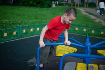 Child on merry-go-round. Boy spins on carousel for children on playground. Junior schoolboy plays alone.