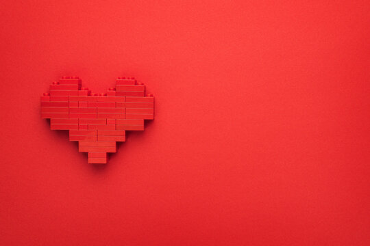 Red heart symbol made of plastic building blocks. Flat lay image of like button on red background with copyspace. Top-down composition of toy heart model. Minimalist photo of stylized red love symbol.
