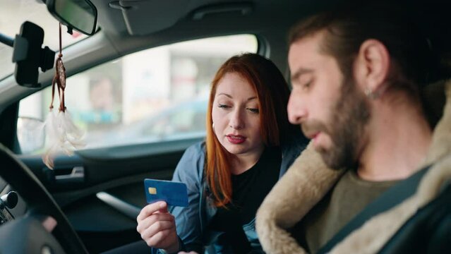 Man and woman couple using smartphone and credit card sitting on car at street