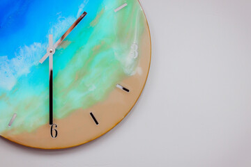 Fototapeta na wymiar Vintage clock handcrafted from wood and epoxy resin. Clock in the form of an ocean shore and a sandy beach. Multi-colored stains of epoxy resin in the form of a finished product.