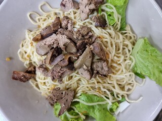 Dried yellow noodles in white cup with chicken offal and a few vegetables.
