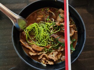 Green noodles with beef and thickened soups and red white chopsticks.