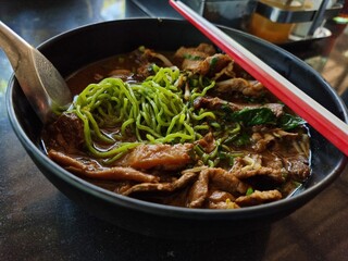 Green noodles with beef and thickened soups and red white chopsticks.