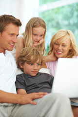 Browsing the web together. Happy young family using a laptop together on the sofa at home.