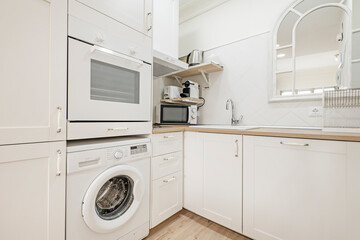 Corner of a kitchen with white wooden cabinets, matching appliances, wooden countertops and a white porcelain sink