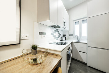 Kitchen cabinets arranged in an L on white bedroom walls with white appliances and a small oak breakfast table © Toyakisfoto.photos