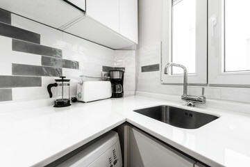 Kitchen cabinets arranged in a corner with white marble countertop, built-in stainless steel sink...
