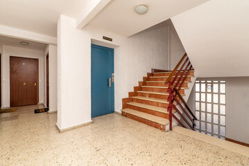 Landing in a residential apartment building with blue metalic elevator door and marble steps on the stairs