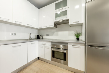 Kitchen with white lacquered furniture with matching stainless steel appliances and gray stone countertop making a corner in the room