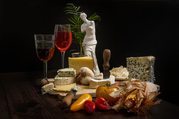 Still life with a wooden board full of delicious cheeses, tomatoes, strong garlic, sweet potatoes,...
