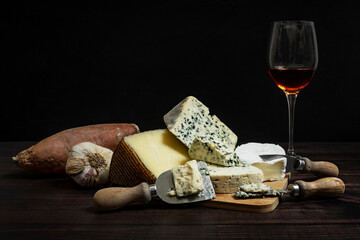 Still life with various kinds of delicious French and Spanish cheeses, garlic and sweet potatoes and a glass of rosé wine