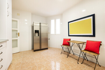 Kitchen with a large stainless steel fridge and a small wooden table with two folding chairs along one wall.