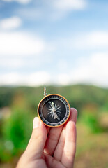 Hand holding a compass with mountains in the background. Using a compass for guidance and...