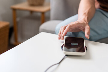 Technology Concept A person with his light blue jeans sitting on the couch and trying to charge his smartphone on the wireless battery charger
