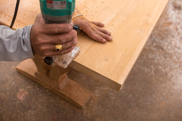 A carpenter uses a laminate trimmer to carefully bevel or smoothen the edge of a table. Furniture...