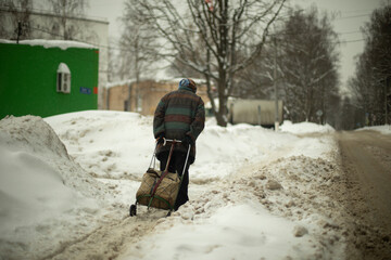 Grandma walks in snow. Woman carries bag on way. Pensioner in city.