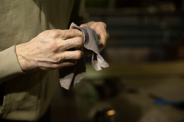 Wipe part with rag. Rag in his hands. Person cleans mechanism from dirt.