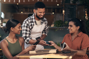 Dont worry, Ive got this one. Shot of two young women sitting at a restaurant and using a credit card machine to pay for their meal.