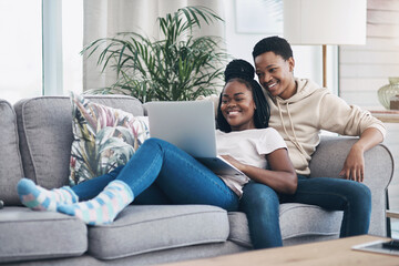Obraz premium Nothing says romance like a cosy weekend at home. Shot of a young couple using a laptop while relaxing on the sofa at home.