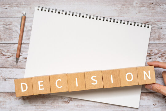 決断のイメージ｜「DECISION」と書かれた積み木、ノート、ペン、人の手