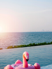 Face of lonely pink flamingo, inflatable ring in the swimming pool on sea and blue sky background with copy space, vertical style. Flamingo swim ring for summer vacation.