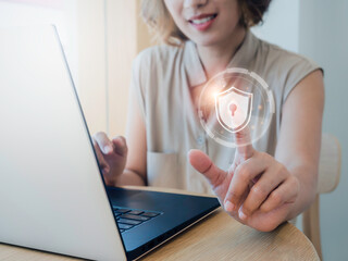 Cyber security, personal data protection, and business privacy concept. Shield and lock icon in the air while woman scanned by her finger for access identification while using laptop computer.