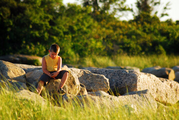 Naklejka na ściany i meble A Young Boy Feeling Alone and Vulnerable sits by himself in a park