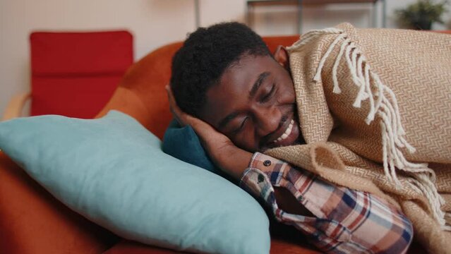 Portrait of african american young man sleeping quietly in bedroom at home. Happy adult guy smiling, lying on bed, sleeping on a comfortable sofa and pillow, resting peacefully. Healthy sleep alone