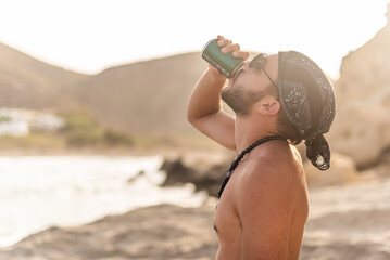 Shirtless man drinking on the shore with light overexposure