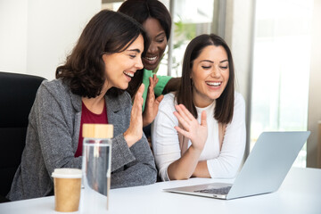 Smiling multiracial coworker women wave hello during business video call using laptop.