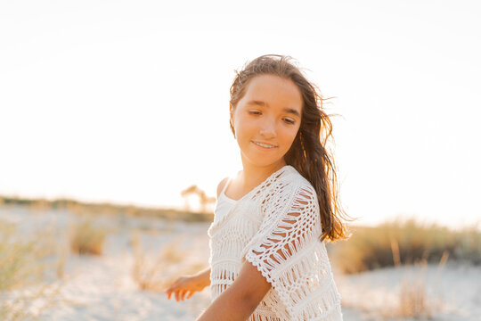  Summer photo of small girl in stylish boho outfit posing on the beach. Warm sunset colors. Wacation and  travel concept.