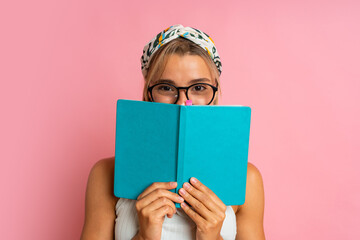Studio photo of pretty blond  student woman with suprice face posing with note book on pink...