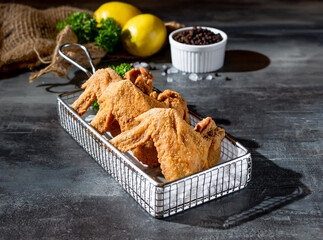 Crispy Chicken Wings in deep fryer with lime and black pepper top view on dark background