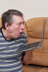 A freak with a surprised face holds a laptop in his hands while sitting on couch - 490997004