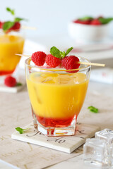 Orange and raspberry cocktail with mint, ice and fresh raspberries on a table
