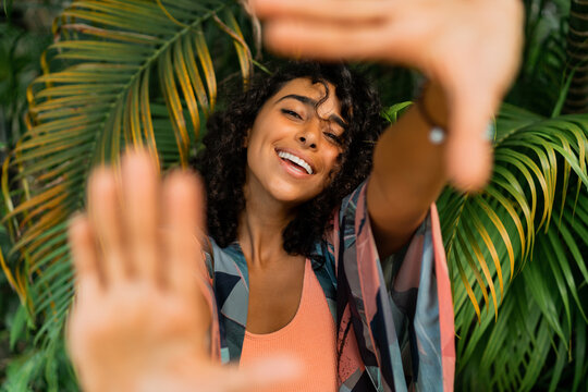 Outdoor  portrait of blissful  lovely woman with curly hairs posing over tropical trees and palm leaves.