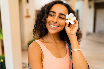 Close up portrait of  beautiful  woman with tropical flower  in hand posing in luxury spa hotel. Spa and body care concept.